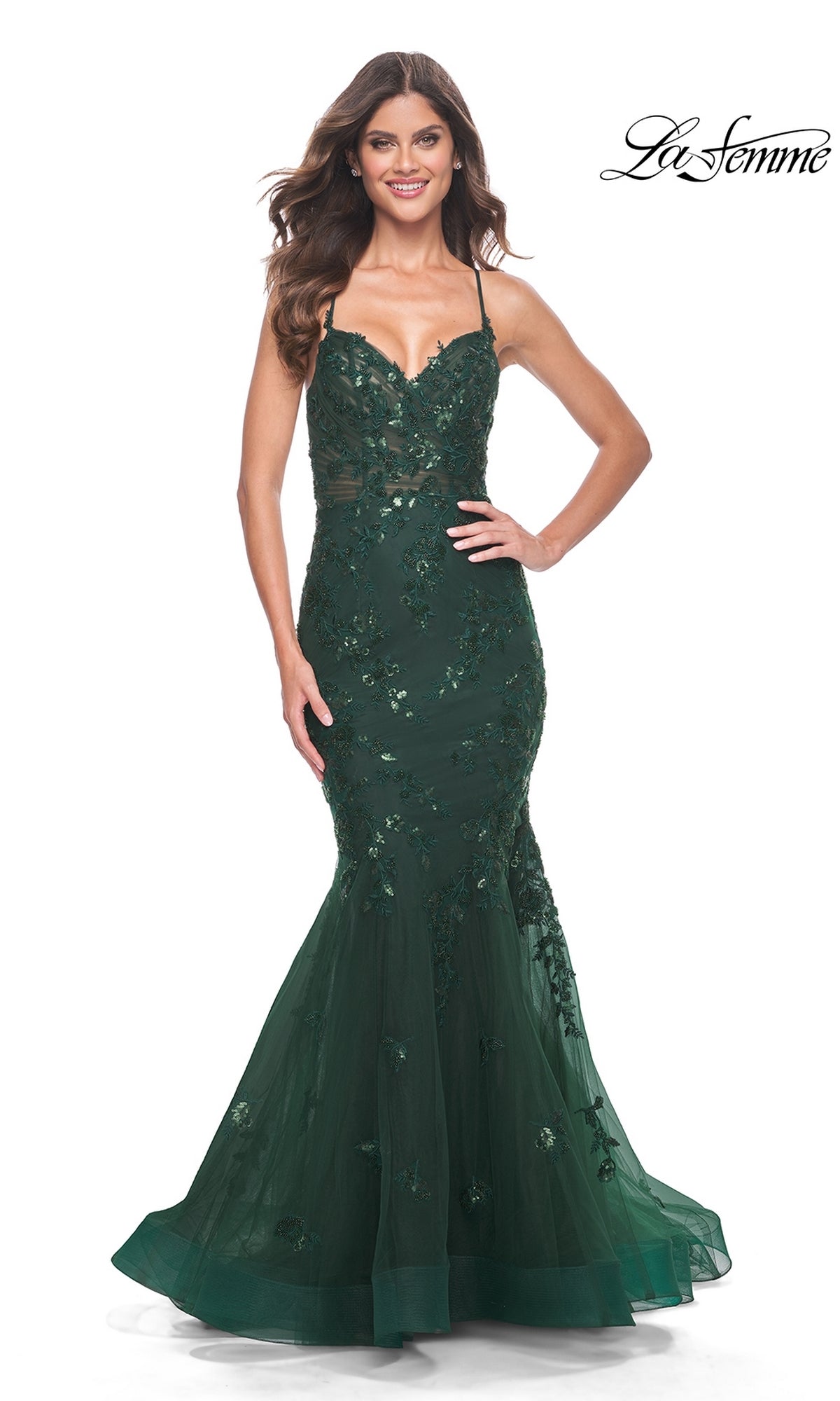 A woman in a dark green La Femme Tonal Lace Long Mermaid Prom Dress 32033 with thin straps and floral beaded lace stands against a white background.